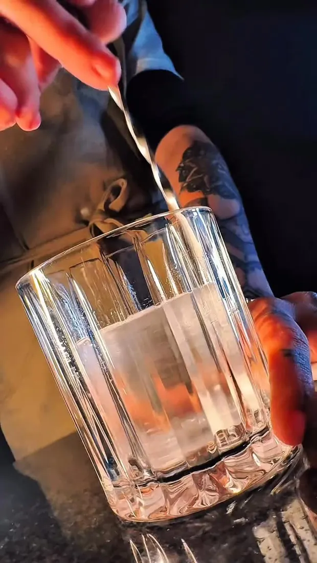 Bartender servindo um drink em copo lapidado