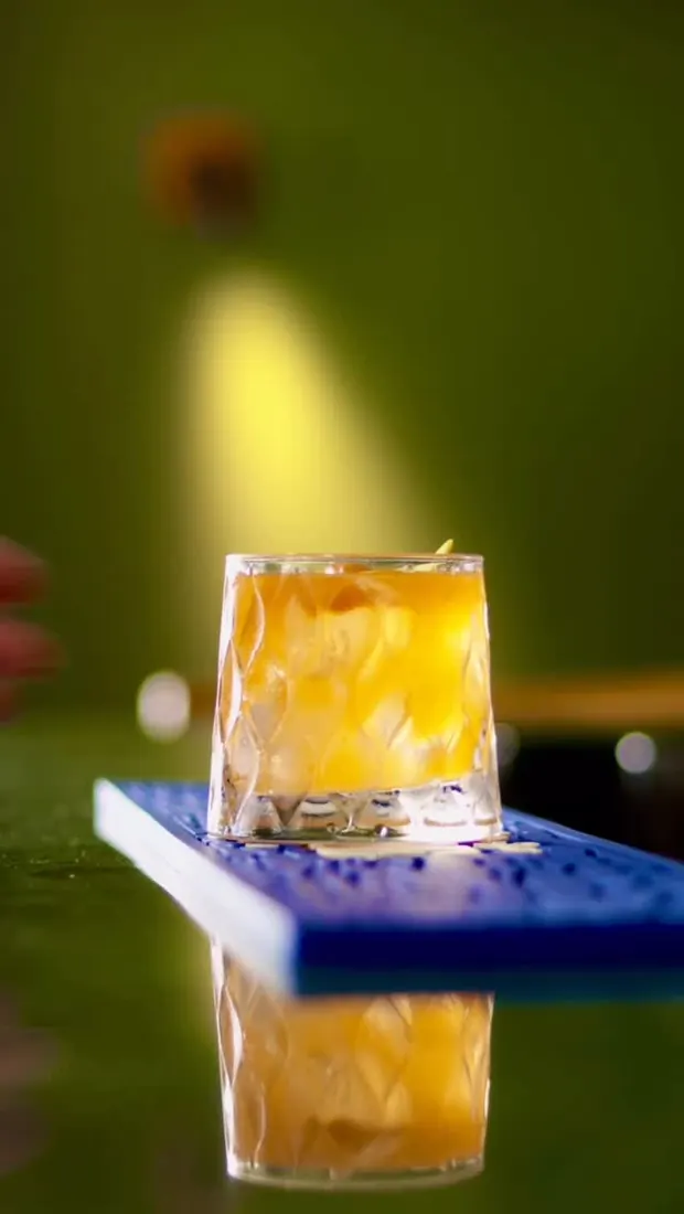 Drink âmbar em copo baixo sobre fundo verde