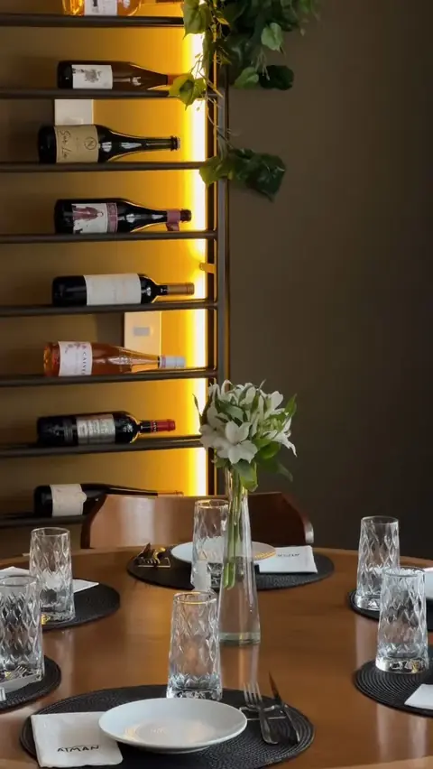 Parede de vinhos iluminada ao lado de uma mesa redonda posta