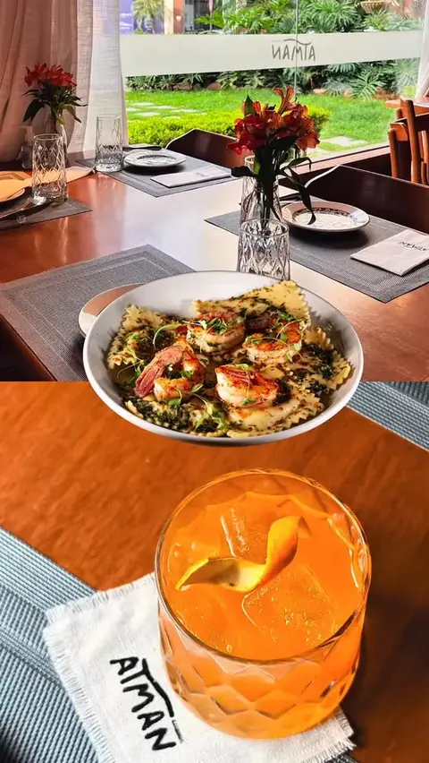 Prato com camarões e drink laranja servidos à mesa, de dia, com o jardim ao fundo