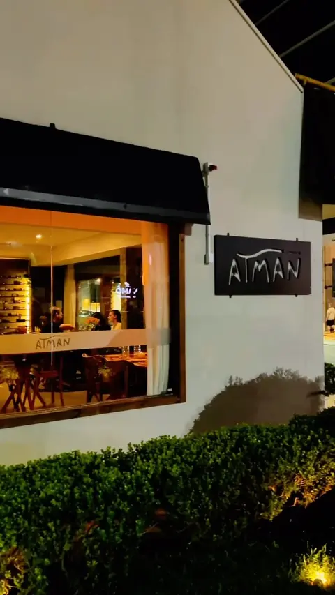 Fachada do Atman iluminada à noite, com a placa e o jardim