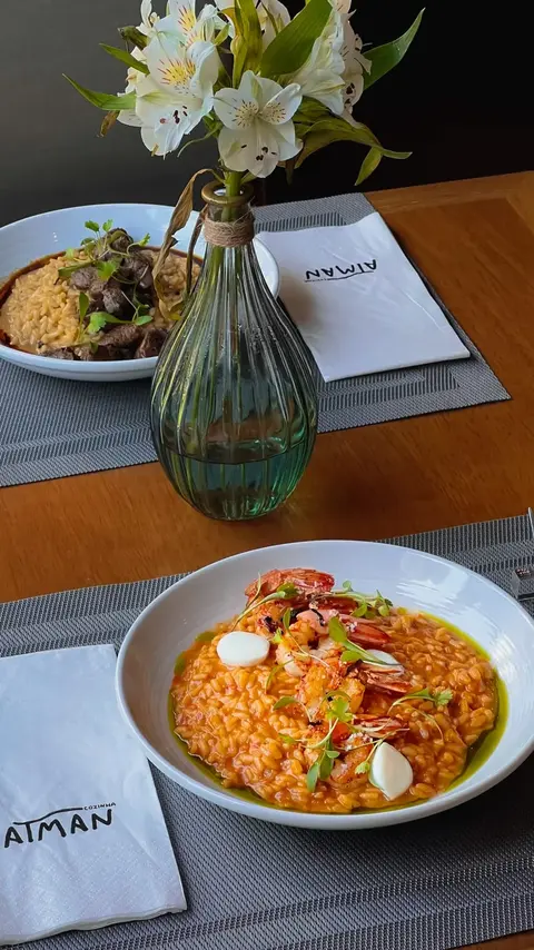 Mesa posta com dois pratos, vaso de flores brancas e guardanapos do Atman